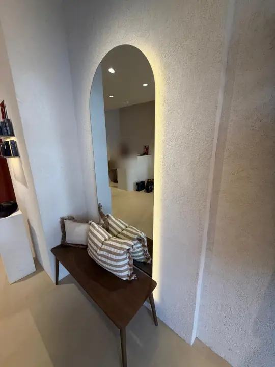 Espejo en arco retroiluminado con LED junto a un banco en un comercio