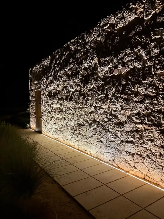 Iluminación rasante de un muro de piedra con tira LED en el suelo